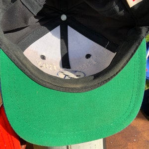 May include: A black and green baseball cap with a white interior. The interior of the cap has the text "Your Trust" printed in black.