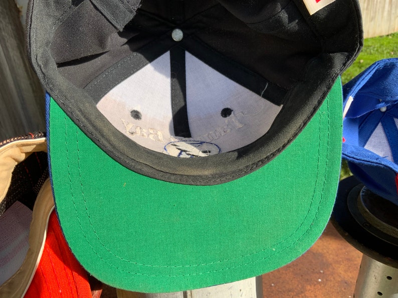 May include: A black and green baseball cap with a white interior. The interior of the cap has the text "Your Trust" printed in black.