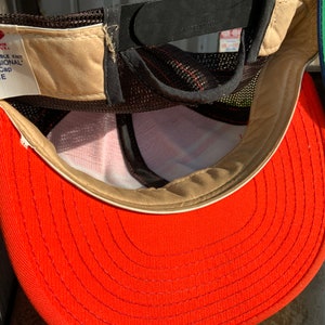 May include: A red baseball cap with a brown mesh back and a white label that reads "100% NYLON - DOUBLE KNIT The "PROFESSIONAL" Baseball Cap LARGE"