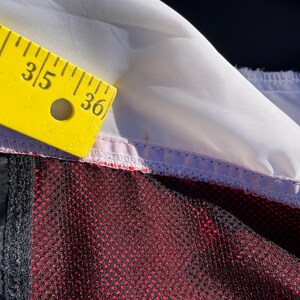 Puede incluir: Una prenda con un panel de tela blanca, una secci&oacute;n negra y una capa de malla roja. Una regla amarilla est&aacute; colocada a lo largo del borde blanco, con la marca de 91,44 cm visible, indicando la medida de la costura del tejido.