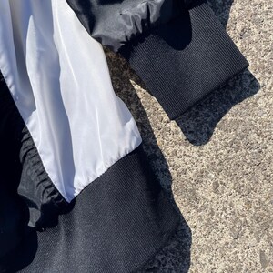 Puede incluir: Primer plano de una chaqueta en blanco y negro. La chaqueta presenta un pu&ntilde;o acanalado negro y un panel blanco. La tela parece ser una combinaci&oacute;n de nailon y punto acanalado. La chaqueta es parcialmente visible, con el foco en la manga y el cuerpo.