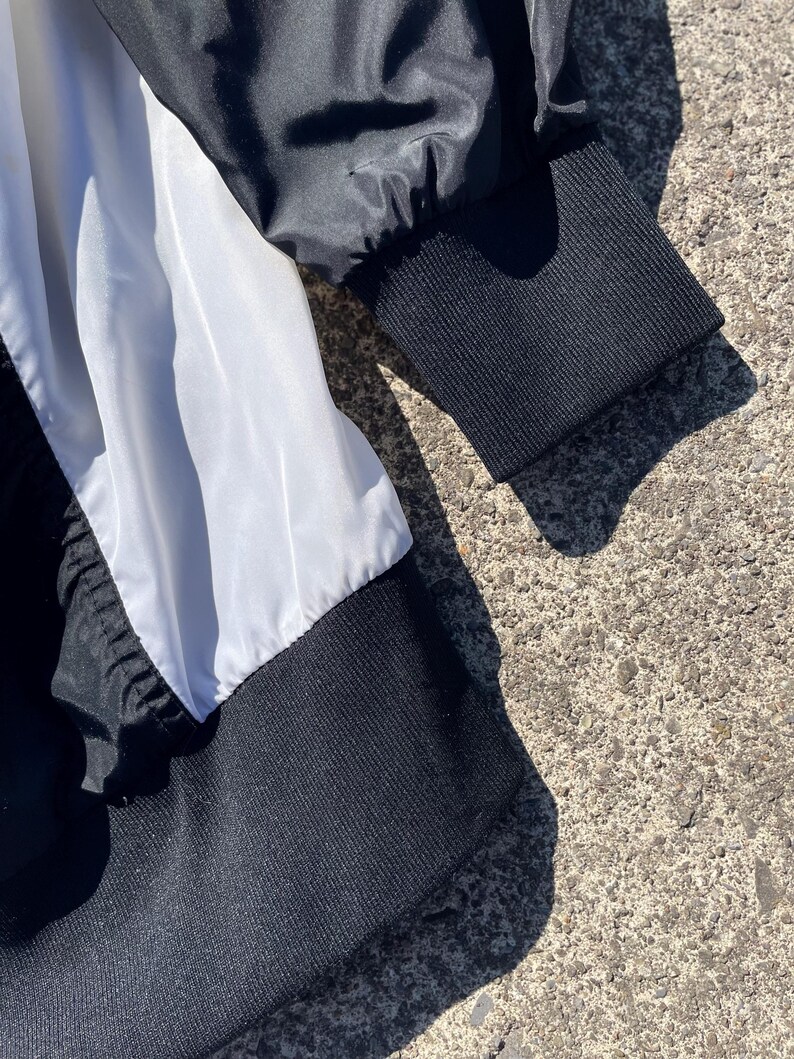Puede incluir: Primer plano de una chaqueta en blanco y negro. La chaqueta presenta un pu&ntilde;o acanalado negro y un panel blanco. La tela parece ser una combinaci&oacute;n de nailon y punto acanalado. La chaqueta es parcialmente visible, con el foco en la manga y el cuerpo.