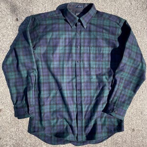 May include: A white ceramic mug with a black handle and the text "But First, Coffee" in a bold, black font. The mug is set against a blurred background, suggesting a cozy setting.