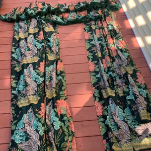May include: Two green and pink patterned curtains with a ruffled top. The curtains feature a floral design with a repeating pattern of birds and plants.