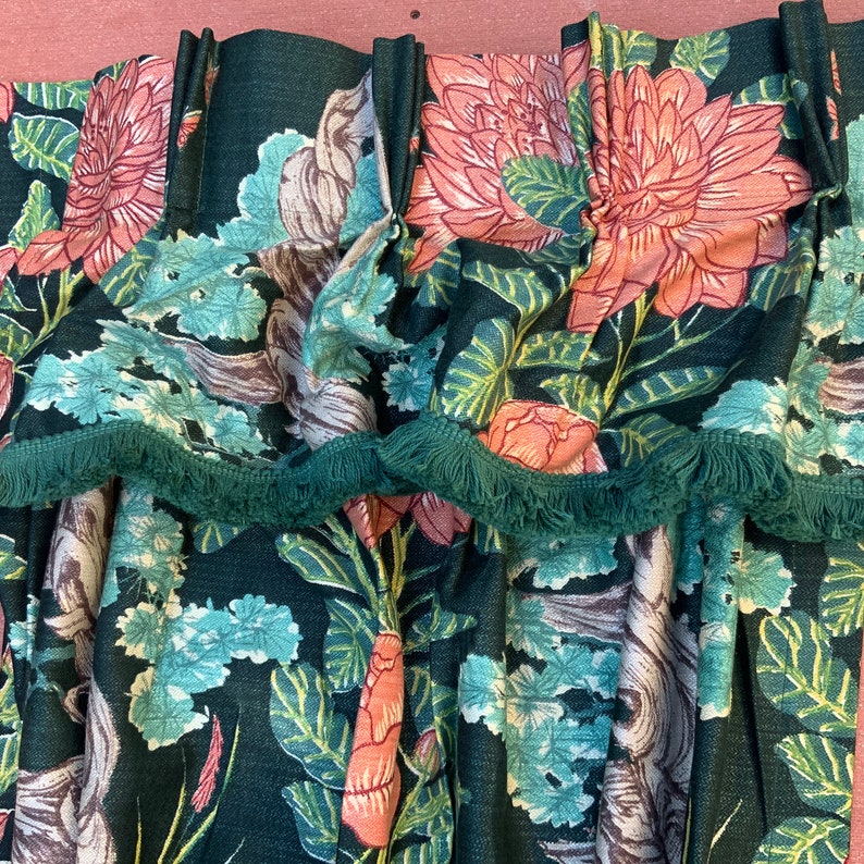 May include: Green fabric with a floral pattern featuring large pink flowers and green leaves. The fabric has a green fringe trim.