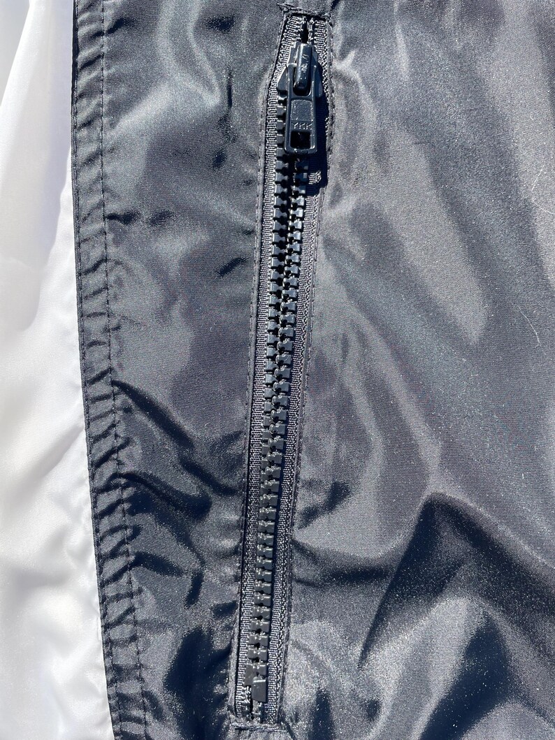 Puede incluir: Primer plano de una chaqueta negra con una cremallera negra. La cremallera est&aacute; centrada y corre verticalmente. La chaqueta tiene una textura brillante y suave. El lado izquierdo de la chaqueta es blanco.
