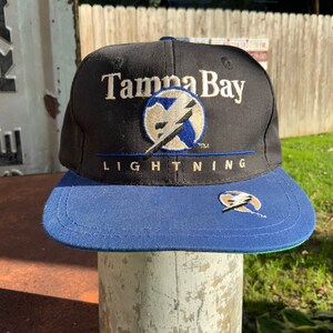May include: A black and blue baseball cap with the embroidered text "Tampa Bay Lightning" and a lightning bolt logo.
