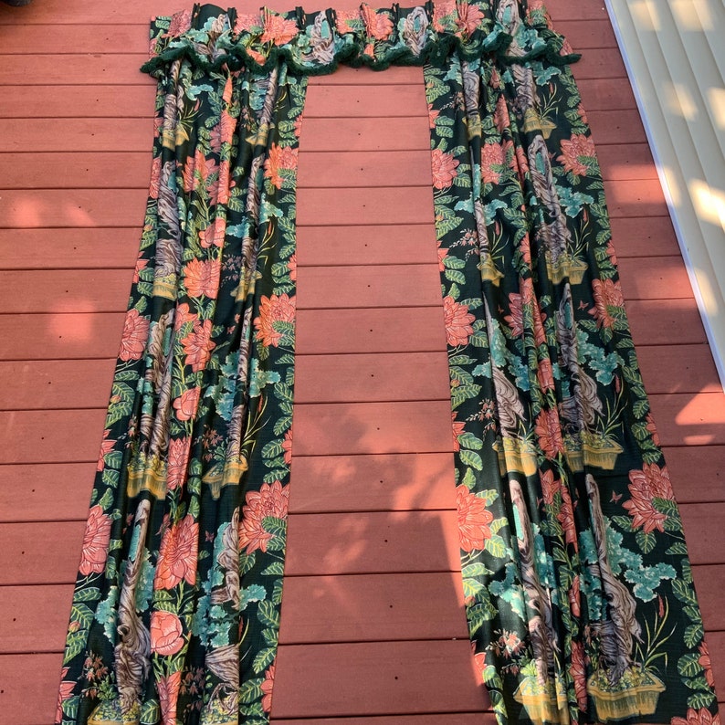 May include: A pair of dark green curtains with a floral print featuring pink flowers, green leaves, and a white background. The curtains have a ruffled top and are hung on a window.