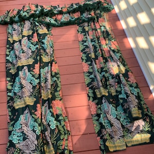 May include: A pair of green curtains with a floral pattern featuring pink flowers, green leaves, and brown tree branches. The curtains have a ruffled top edge.