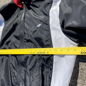Puede incluir: Chaqueta cortavientos Nike negra, blanca y roja con capucha. La chaqueta tiene una franja blanca en las mangas y un peque&ntilde;o logotipo de Nike en el pecho. La chaqueta mide aproximadamente 56 cm de ancho.