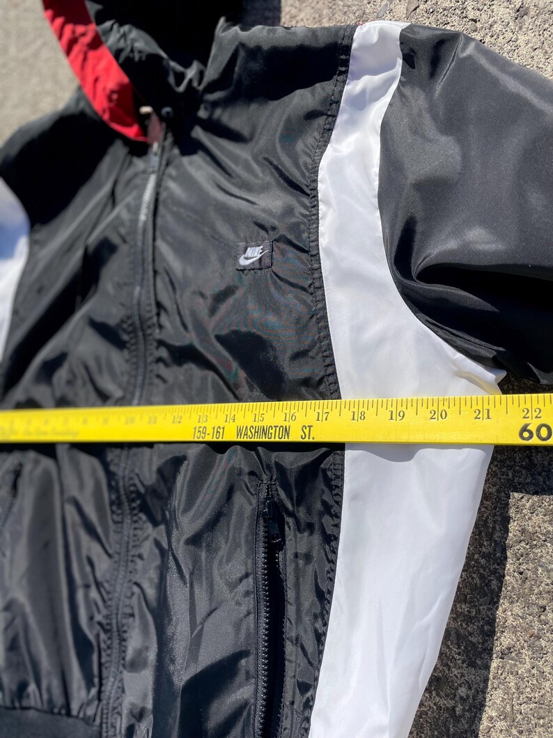 Puede incluir: Chaqueta cortavientos Nike negra, blanca y roja con capucha. La chaqueta tiene una franja blanca en las mangas y un peque&ntilde;o logotipo de Nike en el pecho. La chaqueta mide aproximadamente 56 cm de ancho.