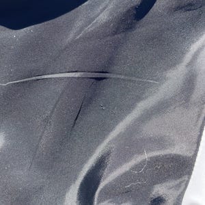 Puede incluir: Primer plano de una tela negra con una textura suave y ligeramente brillante. La tela tiene pliegues y arrugas sutiles, creando sombras y reflejos. La imagen est&aacute; bien iluminada, mostrando los detalles del material.