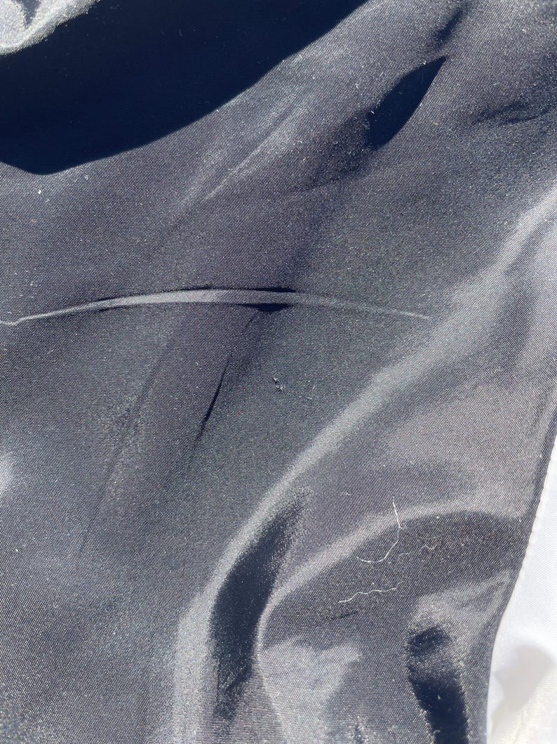 Puede incluir: Primer plano de una tela negra con una textura suave y ligeramente brillante. La tela tiene pliegues y arrugas sutiles, creando sombras y reflejos. La imagen est&aacute; bien iluminada, mostrando los detalles del material.