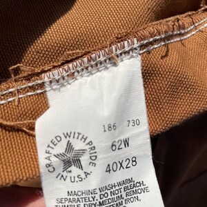 May include: Close-up of a brown fabric label with white stitching. The label reads "CRAFTED WITH PRIDE IN U.S.A." and includes the measurements "40X28" and "62W". The label also includes washing instructions.
