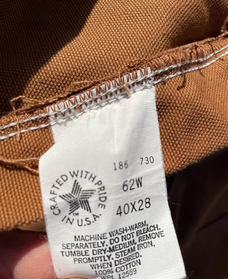 May include: Close-up of a brown fabric label with white stitching. The label reads "CRAFTED WITH PRIDE IN U.S.A." and includes the measurements "40X28" and "62W". The label also includes washing instructions.