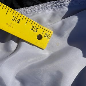 Puede incluir: Una regla amarilla, marcada en pulgadas, descansa sobre una tela gris claro. La regla muestra medidas de 83,8 a 91,4 cm. La tela tiene un brillo sutil y est&aacute; ligeramente arrugada.