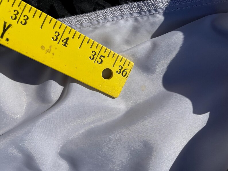 Puede incluir: Una regla amarilla, marcada en pulgadas, descansa sobre una tela gris claro. La regla muestra medidas de 83,8 a 91,4 cm. La tela tiene un brillo sutil y est&aacute; ligeramente arrugada.