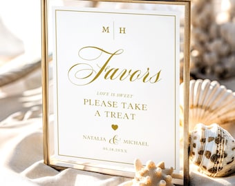 Op de afbeelding: Een rechthoekige goudkleurige metalen lijst met een wit bordje met gouden tekst die luidt M H, Favors, LOVE IS SWEET PLEASE TAKE A TREAT, een hartsymbool, NATALIA & MICHAEL en 06.18.20XX. Het bordje heeft een dunne gouden rand.