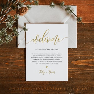 May include: A white welcome sign with gold calligraphy that reads "welcome". The sign also includes the text "Dear family and friends, We are thrilled that you are here to share the joy of our wedding celebration. We are so fortunate to have each and every one of you in our lives and are honoured that you have travelled to be with us. We hope you enjoy your stay and the weekend's festivities. Riley + Brian".
