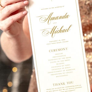Pu&ograve; includere: Un programma di cerimonia di matrimonio bianco con lettere dorate. Il programma elenca l'ordine degli eventi per il matrimonio di Amanda e Michael, che si terr&agrave; il 18 settembre 20XX a Clear Water Beach, in Florida.