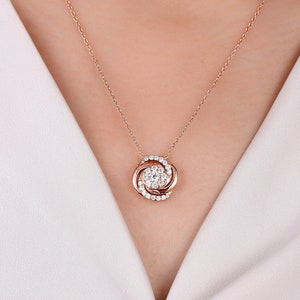 May include: A rose gold necklace with a round pendant featuring a cluster of small diamonds in a swirl design.
