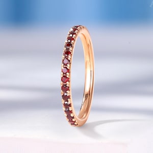 May include: A rose gold band ring with a row of small red gemstones around the entire band.
