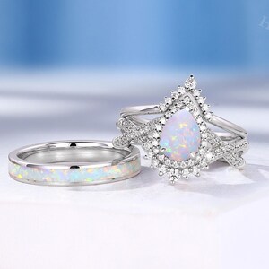 May include: A pear-shaped opal engagement ring set with a halo of smaller diamonds. The ring is set on a silver band and is accompanied by a matching opal and diamond wedding band.