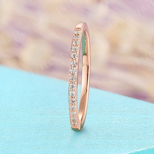 May include: A rose gold band ring with small, clear gemstones set along the top. The ring is displayed on a light blue surface. The brand name "HELLORING FINE JEWELRY" is visible in the upper left corner.