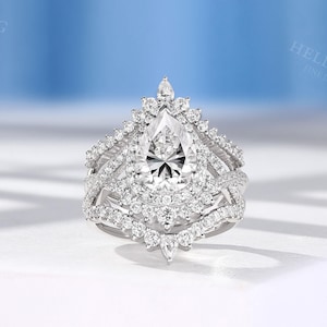 May include: A pear-shaped diamond engagement ring with a halo setting and a delicate, intricate band. The ring is set in white gold and features a large, sparkling centre stone.