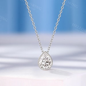 May include: A silver chain necklace with a pear-shaped diamond pendant. The pendant has a halo of smaller diamonds around it.