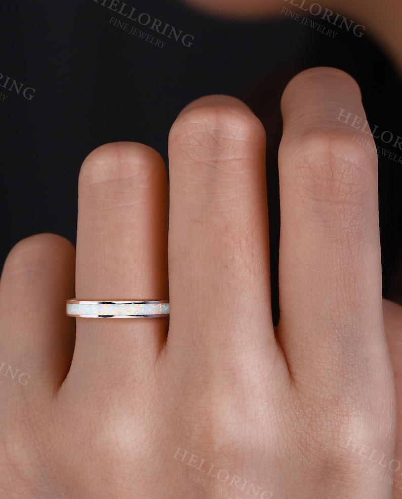 May include: A thin silver band ring with a white opal inlay. The ring is on a person's finger.