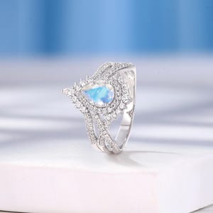 Peut inclure: Une bague en argent avec une pierre pr&eacute;cieuse en forme de poire et un sertissage halo. La bague est en argent et poss&egrave;de une pierre pr&eacute;cieuse blanche au centre. La bague est pos&eacute;e sur un fond blanc.