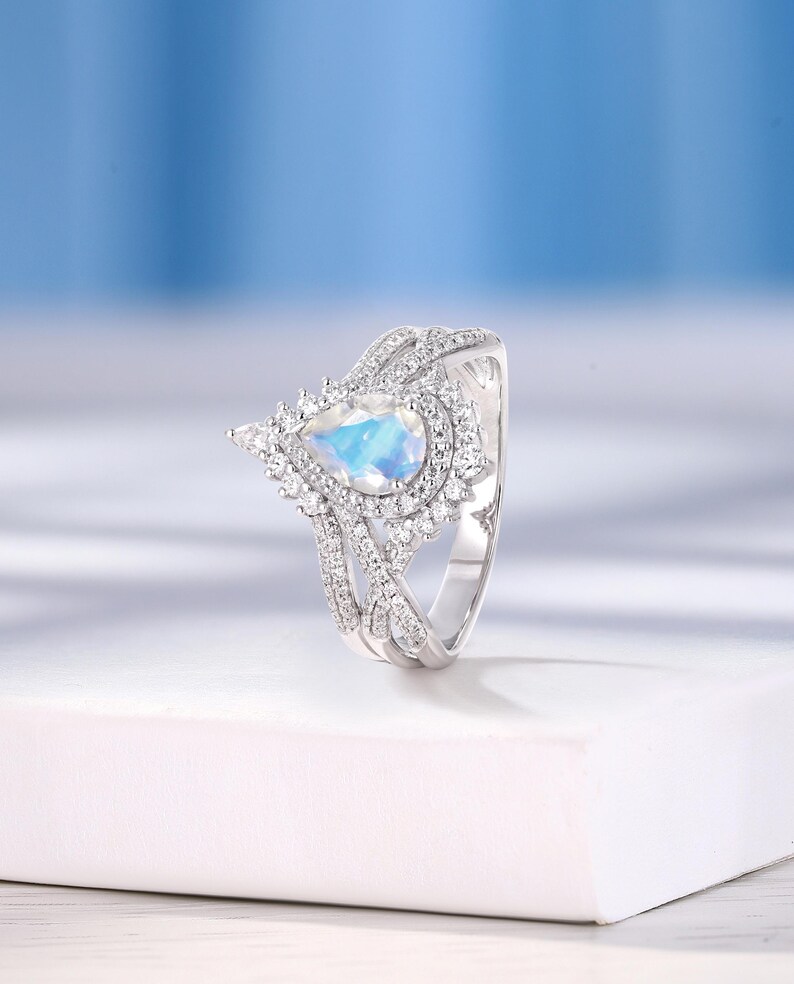 Peut inclure: Une bague en argent avec une pierre pr&eacute;cieuse en forme de poire et un sertissage halo. La bague est en argent et poss&egrave;de une pierre pr&eacute;cieuse blanche au centre. La bague est pos&eacute;e sur un fond blanc.