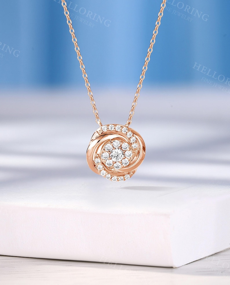 May include: A rose gold necklace with a round pendant featuring a cluster of small diamonds in a swirl design.
