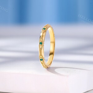 May include: A yellow gold band ring featuring a series of small, round, green gemstones set within decorative, diamond-shaped metal frames. The band has a polished finish and intricate milgrain detailing along the edges of the settings.