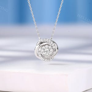 May include: A silver necklace with a round pendant featuring a cluster of small diamonds set in a swirling design.