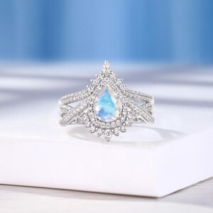 Peut inclure: Une bague de fian&ccedil;ailles en argent avec une pierre de lune en forme de poire et un halo de diamants plus petits. La bague est de conception d&eacute;licate et complexe.