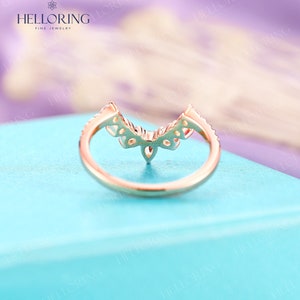 May include: A delicate gold ring with a V-shaped design featuring small diamonds. The ring is on a light blue background.