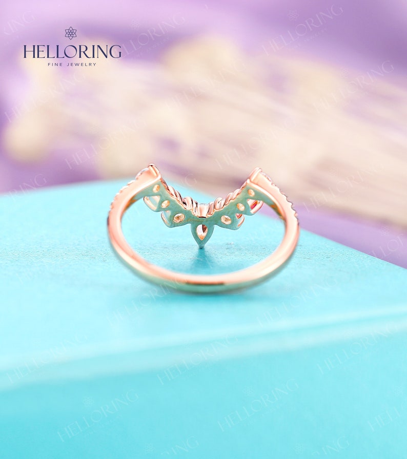 May include: A delicate gold ring with a V-shaped design featuring small diamonds. The ring is on a light blue background.