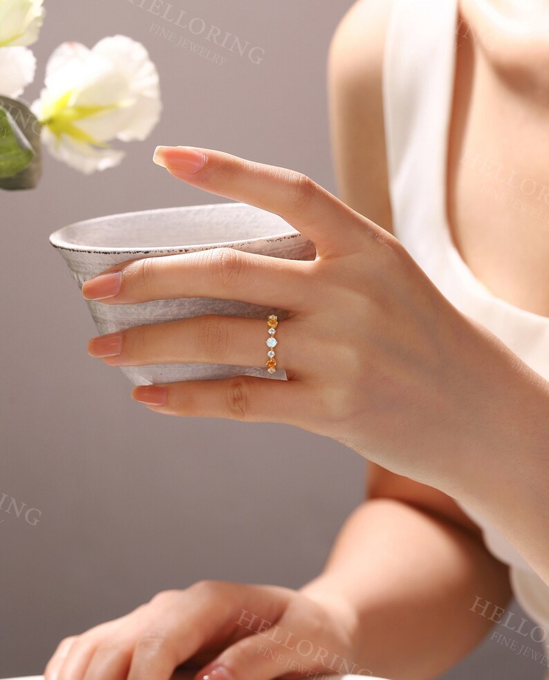 May include: A gold band ring with alternating clear and orange gemstones. The ring is worn on a person's finger.