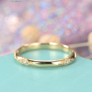 May include: A thin gold wedding band with a delicate diamond pattern. The band is on a light blue background.