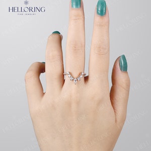 May include: A delicate gold ring with a V-shaped design featuring a row of small round diamonds and a larger pear-shaped diamond at the center.