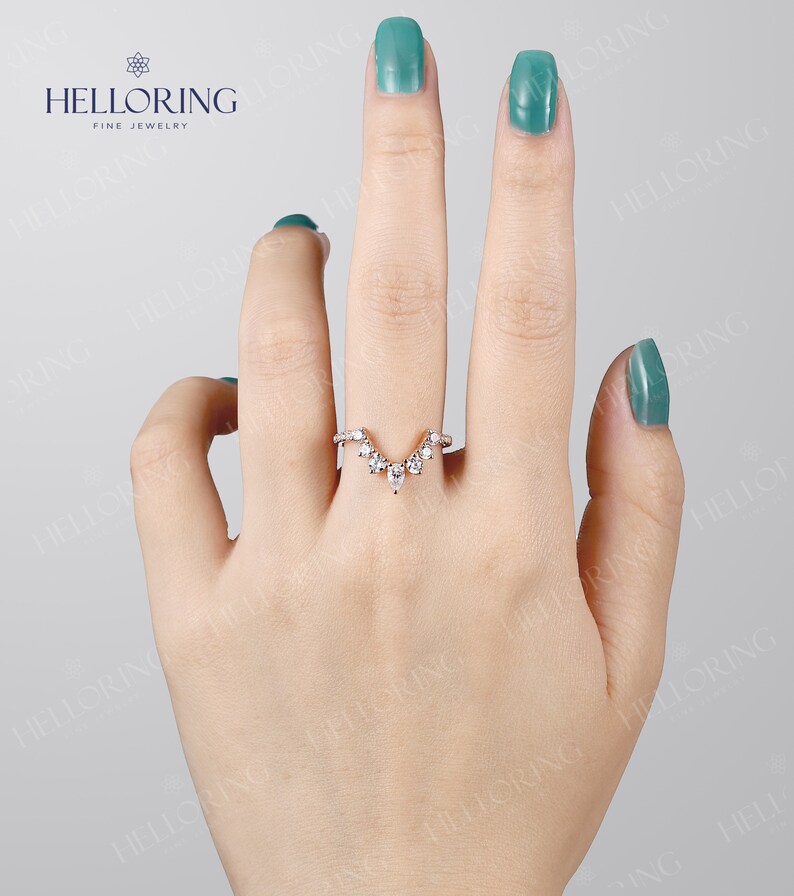 May include: A delicate gold ring with a V-shaped design featuring a row of small round diamonds and a larger pear-shaped diamond at the center.