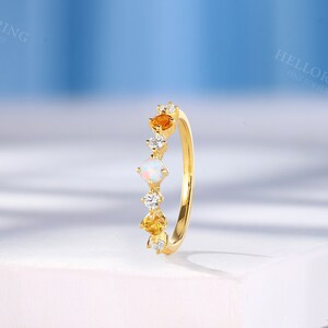 May include: A gold band ring with a row of gemstones. The ring features a white opal, two yellow gemstones, and small clear gemstones.