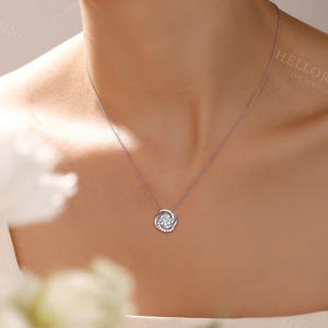 May include: A silver necklace with a small, round pendant featuring a swirl design with clear gemstones. The pendant is on a delicate chain.