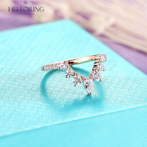 May include: A rose gold wedding band with a delicate, v-shaped design featuring a row of small round diamonds and a cluster of larger pear-shaped diamonds.