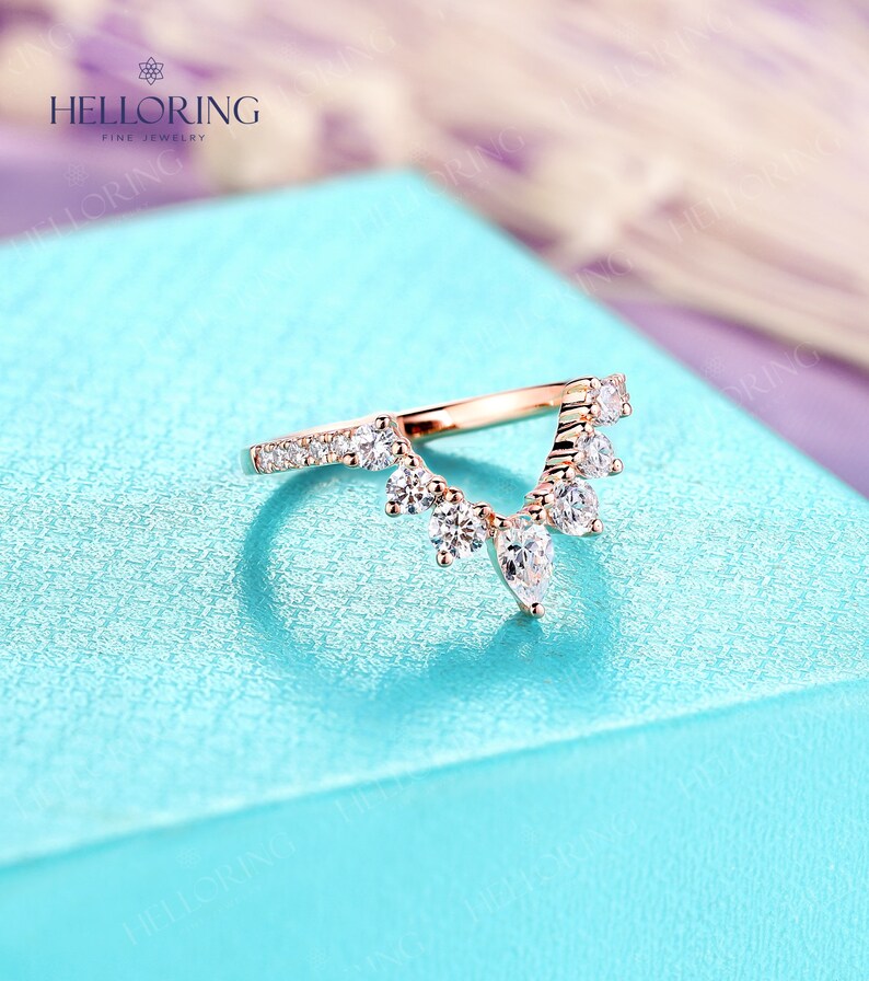 May include: A rose gold wedding band with a delicate, v-shaped design featuring a row of small round diamonds and a cluster of larger pear-shaped diamonds.