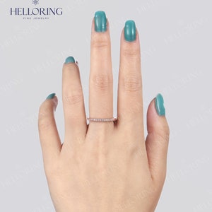 May include: A rose gold band ring with small, clear gemstones set across the top. The ring is displayed on a hand with turquoise nail polish. The ring is from the brand HELLORING FINE JEWELRY.