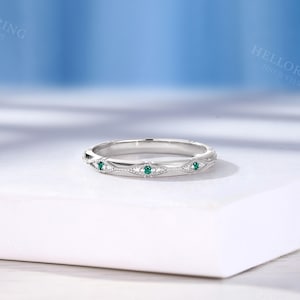 May include: A silver-toned metal band ring featuring a series of marquise-shaped engravings, each set with a small, round, vibrant green gemstone. The band displays intricate milgrain detailing along the edges of the marquise motifs.