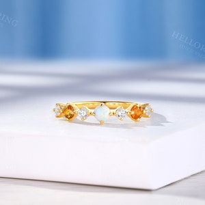May include: A gold band ring with a white opal and small yellow gemstones. The ring is on a white surface.